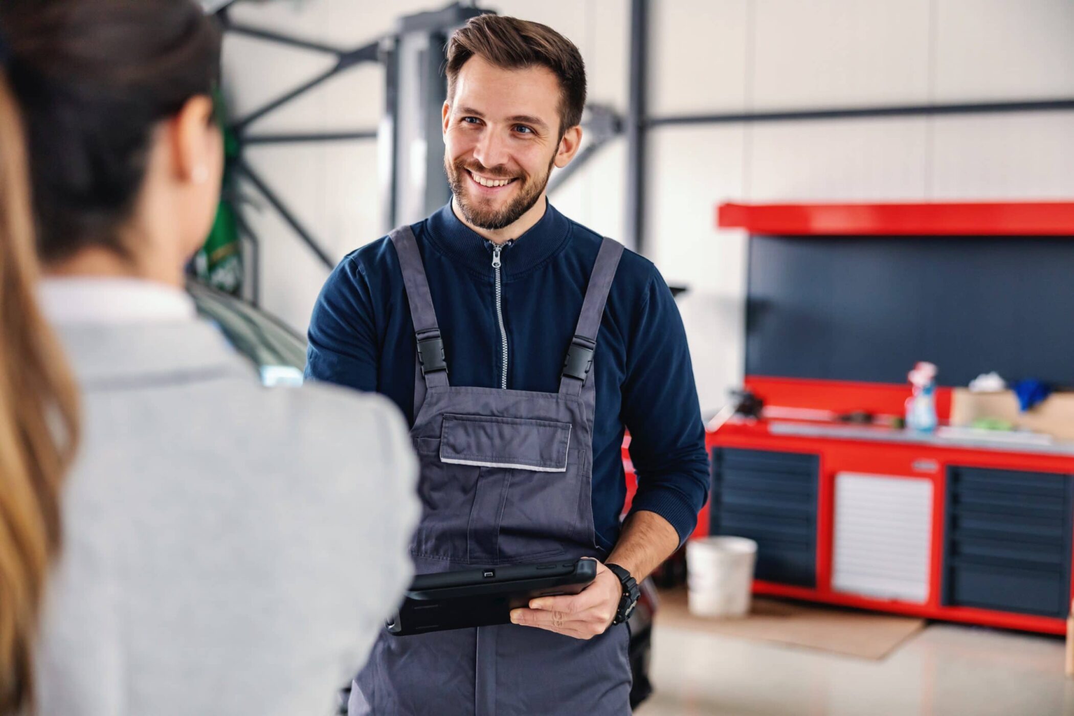 Smiling friendly car seller talking to a mechanic and showing okay hand gesture while standing in car salon.