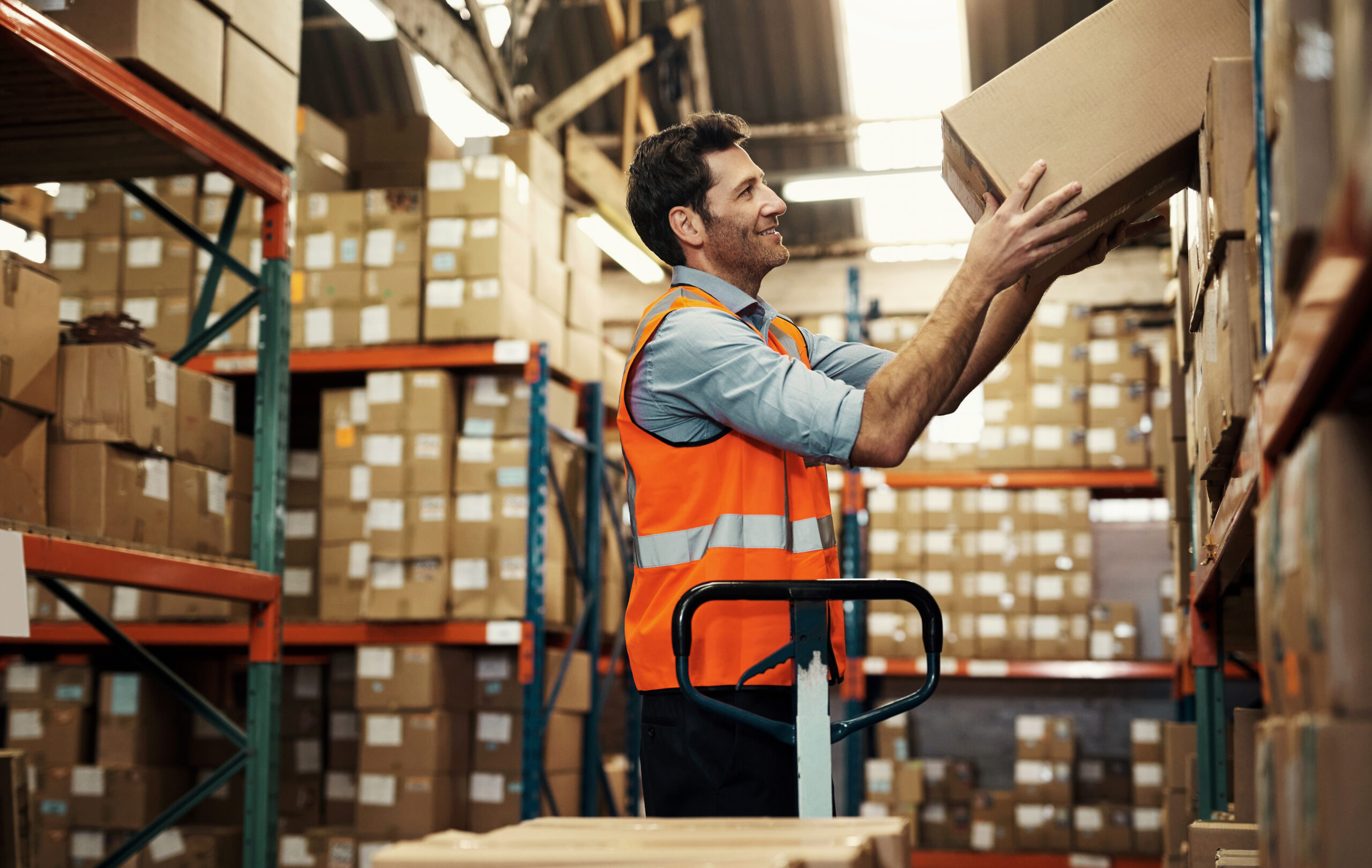 Warehouse, boxes and man unloading shelf for stock, inventory or distribution. Happy, worker and person taking box for logistics, storage or package for shipping, cargo or freight for supply chain.