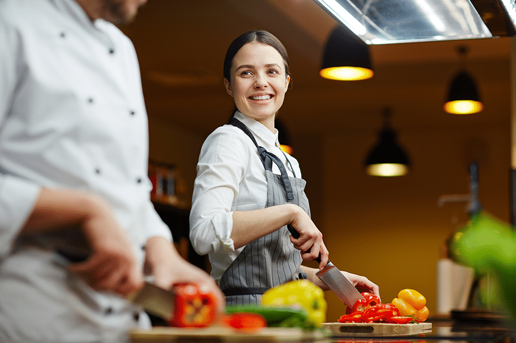 Food prep assistant smiling at chef while prepping